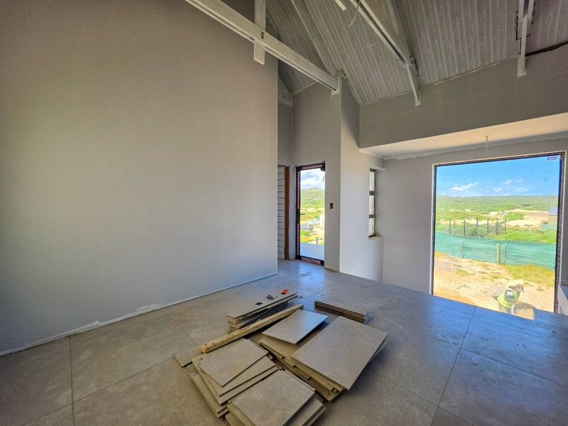 An unfinished living area featuring vaulted ceilings with exposed rafters, large windows, and tiled flooring, currently undergoing final construction and finishing work.