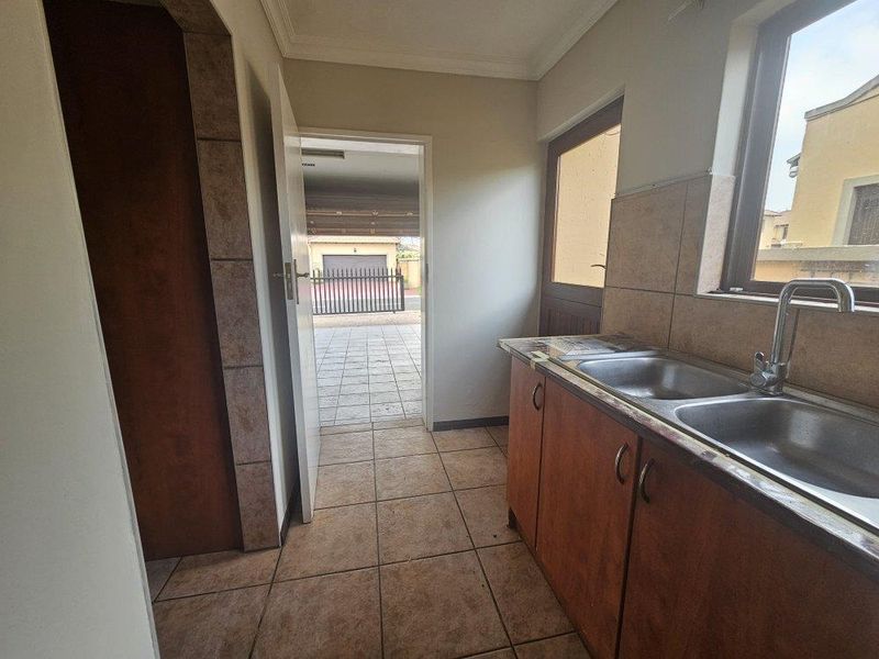 A functional scullery area featuring a double basin sink, tiled splashbacks, and built-in cabinetry, with direct access to the exterior driveway.