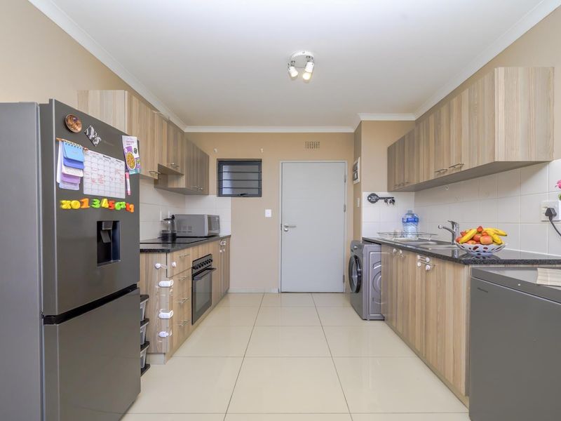 A well-maintained kitchen featuring light wood-finish cabinetry, granite countertops, integrated oven and hob, and neutral tiled flooring.