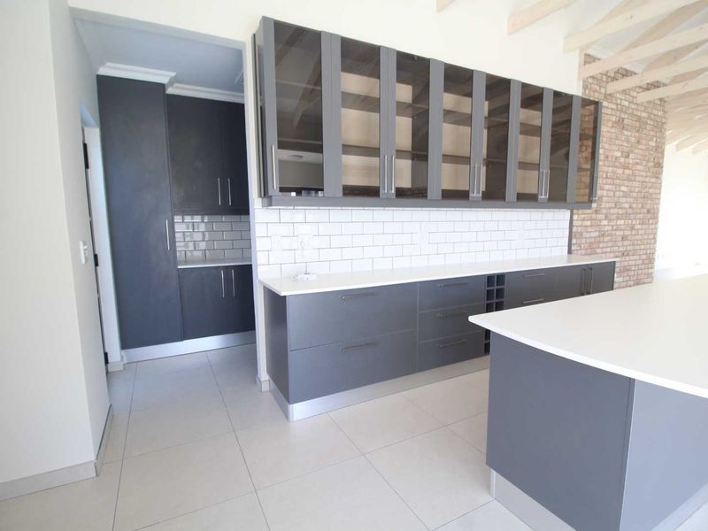 Modern kitchen featuring dark grey cabinetry, white subway tile backsplash, stone countertops, a central island, and exposed brickwork with timber ceiling beams.