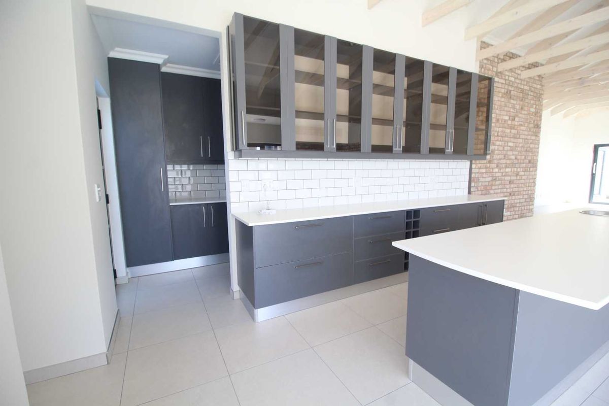 Modern kitchen featuring dark grey cabinetry, white subway tile backsplash, stone countertops, a central island, and exposed brickwork with timber ceiling beams.