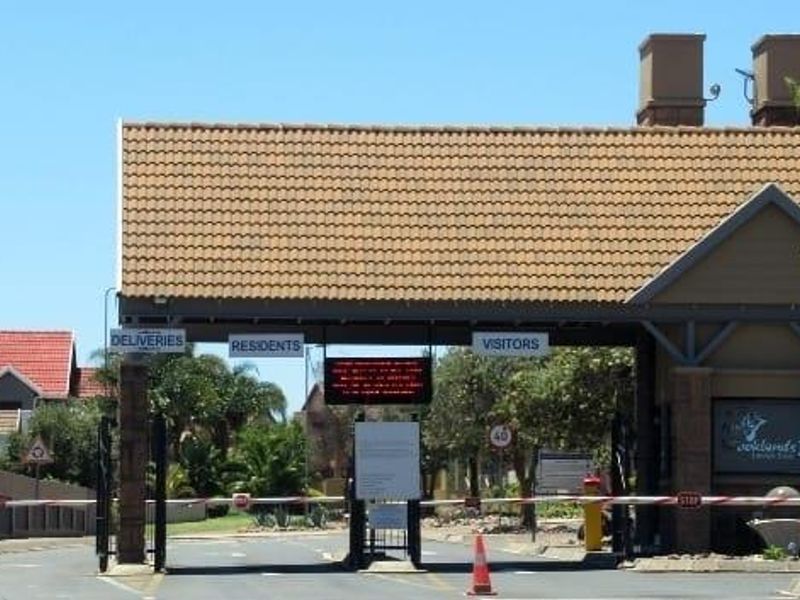 The entrance gate to the residential estate featuring a tiled roof structure, security boom gates, and designated lanes for residents, visitors, and deliveries.