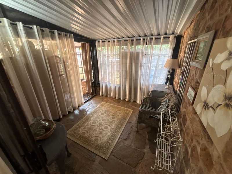 A rustic enclosed patio featuring natural stone flooring, an exposed stone feature wall, and a corrugated metal ceiling with large windows.