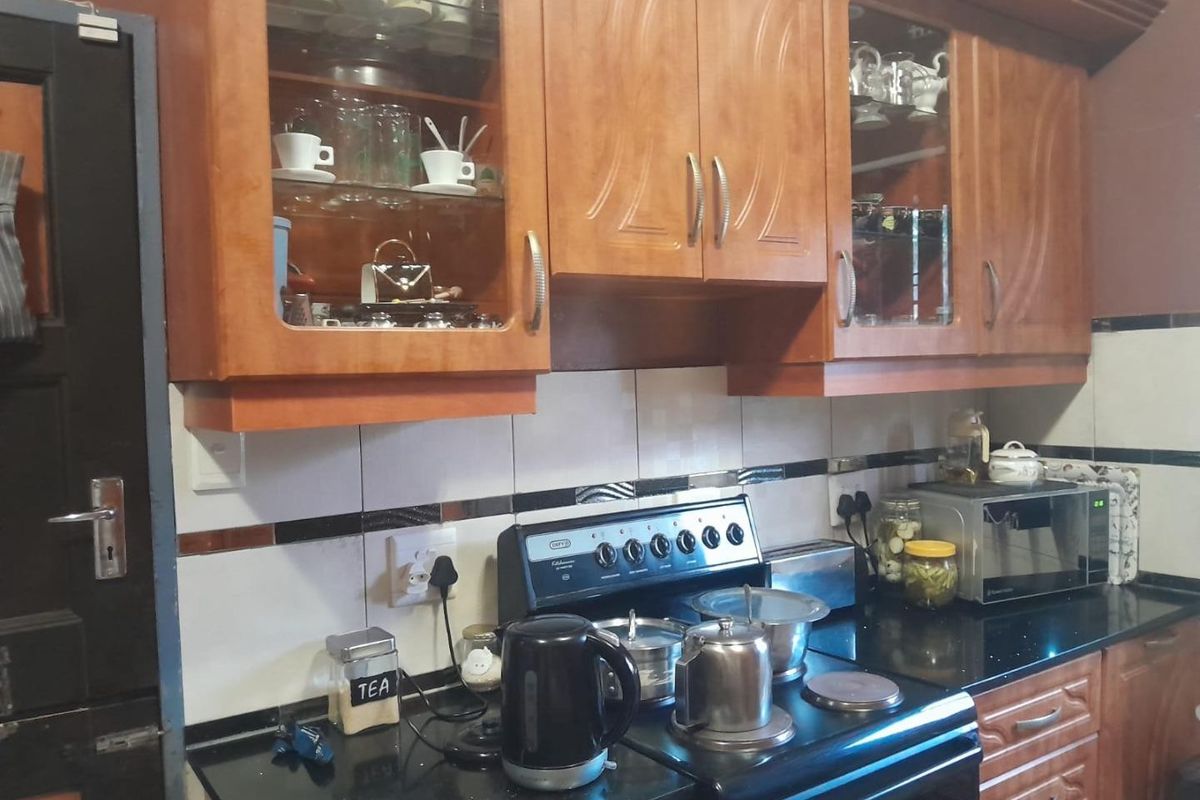A functional kitchen featuring warm-toned wooden cabinetry, black granite countertops, and a classic freestanding stove with tiled splashbacks.