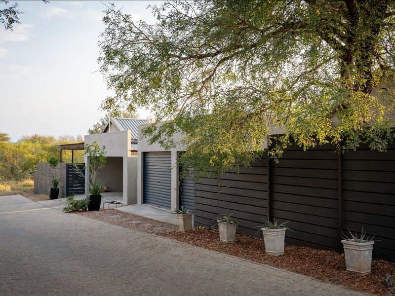 Modern residential exterior featuring a paved driveway, integrated garage, and contemporary timber slat fencing set against a natural landscape.