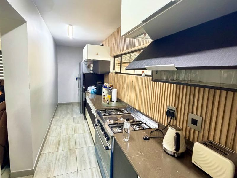 Modern galley-style kitchen featuring stone countertops, gas cooktop, integrated extractor fan, and stylish slatted wood wall paneling with neutral floor tiles.