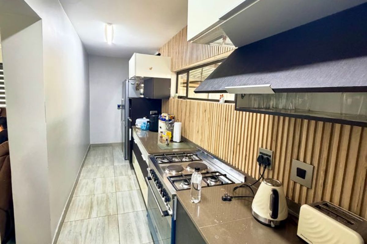 Modern galley-style kitchen featuring stone countertops, gas cooktop, integrated extractor fan, and stylish slatted wood wall paneling with neutral floor tiles.