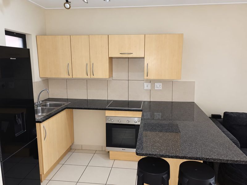 A functional kitchen featuring light wood cabinetry, dark granite countertops, a built-in oven, electric hob, and a double sink with tiled backsplash.