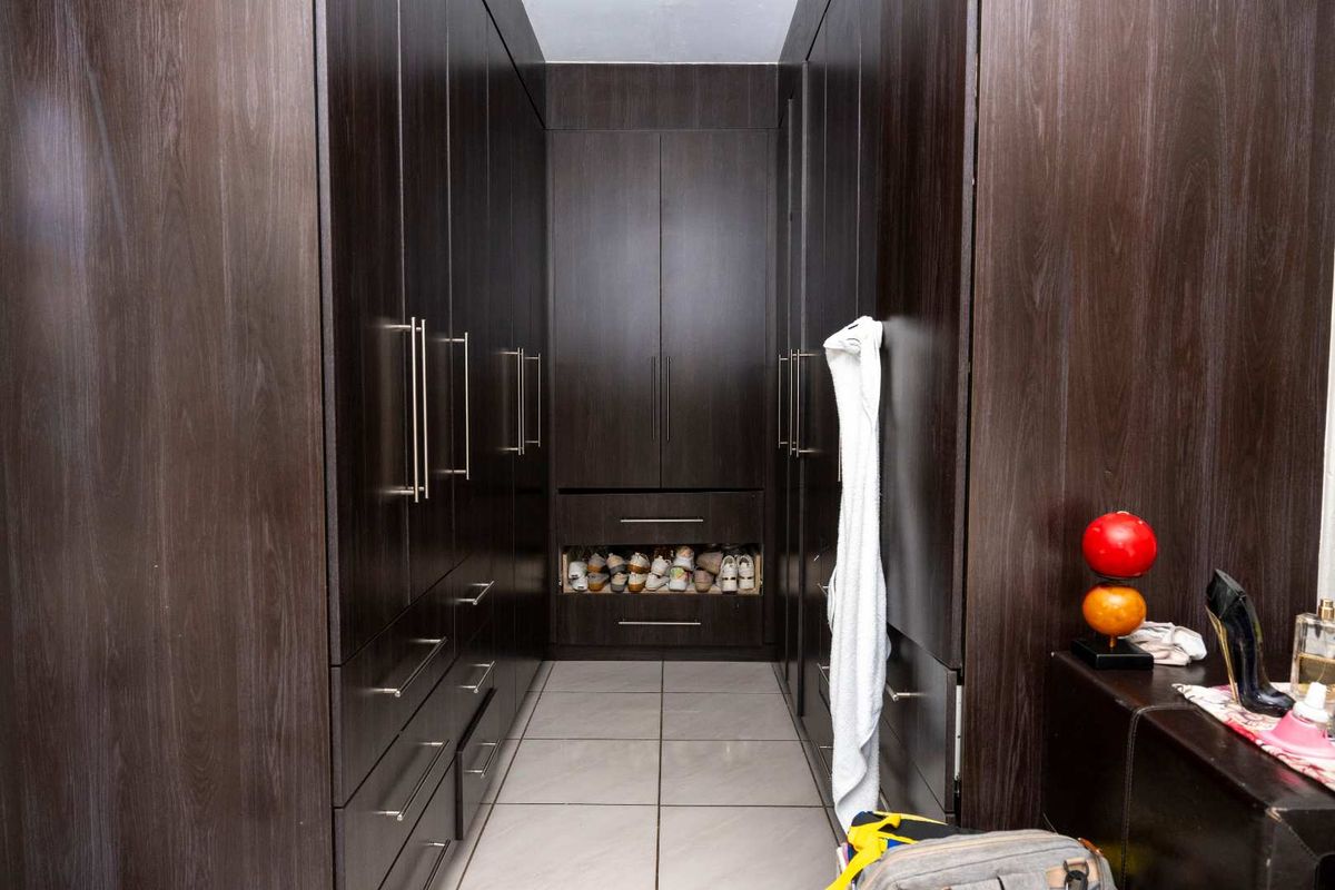 A walk-in closet featuring extensive dark wood cabinetry with integrated drawers and shelving, complemented by neutral floor tiling.