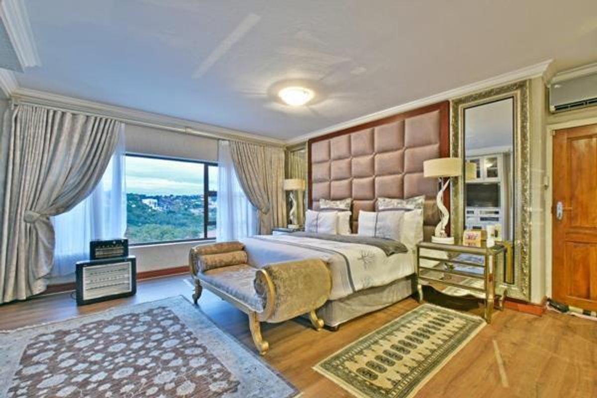 Spacious bedroom featuring a large window with scenic views, a custom upholstered headboard, and wood-look flooring.