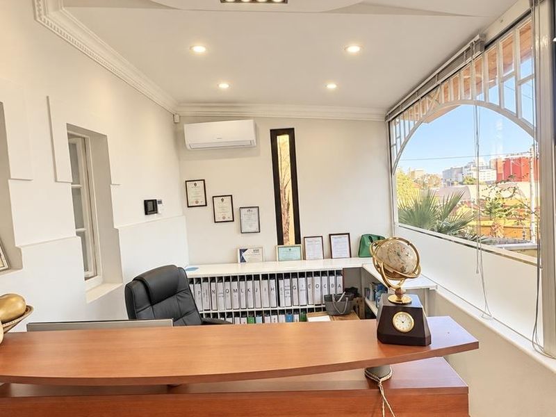 A well-lit professional office space featuring built-in cabinetry, recessed ceiling lighting, a split-system air conditioner, and a large arched window with exterior views.