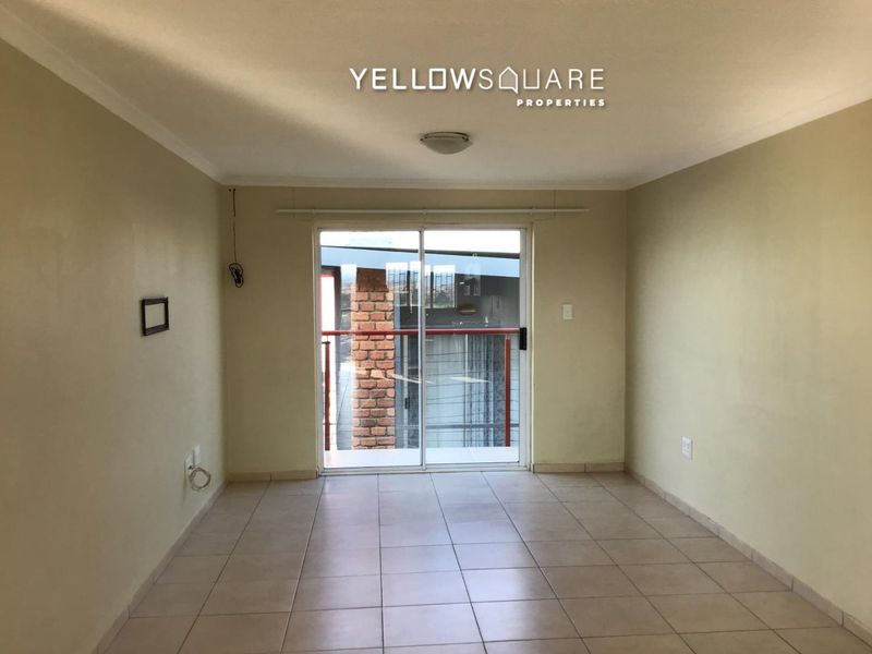 An empty living room featuring ceramic floor tiles, neutral walls, and a sliding glass door providing access to an outdoor balcony area.