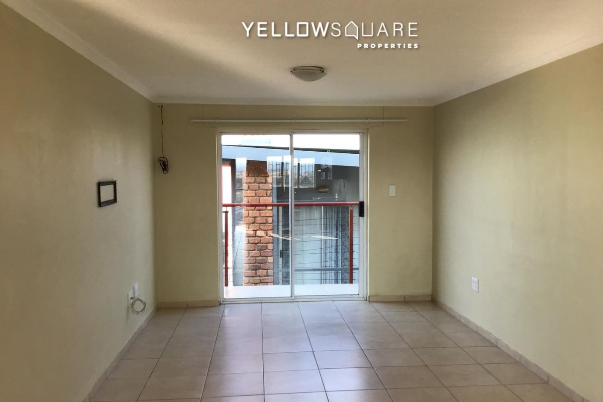 An empty living room featuring ceramic floor tiles, neutral walls, and a sliding glass door providing access to an outdoor balcony area.
