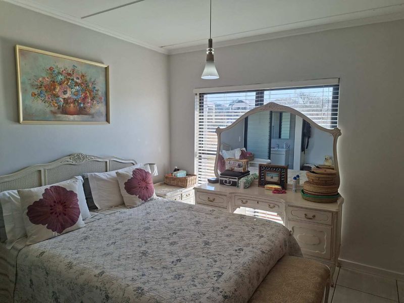 A well-lit bedroom featuring tiled flooring, neutral wall finishes, and large windows fitted with venetian blinds.