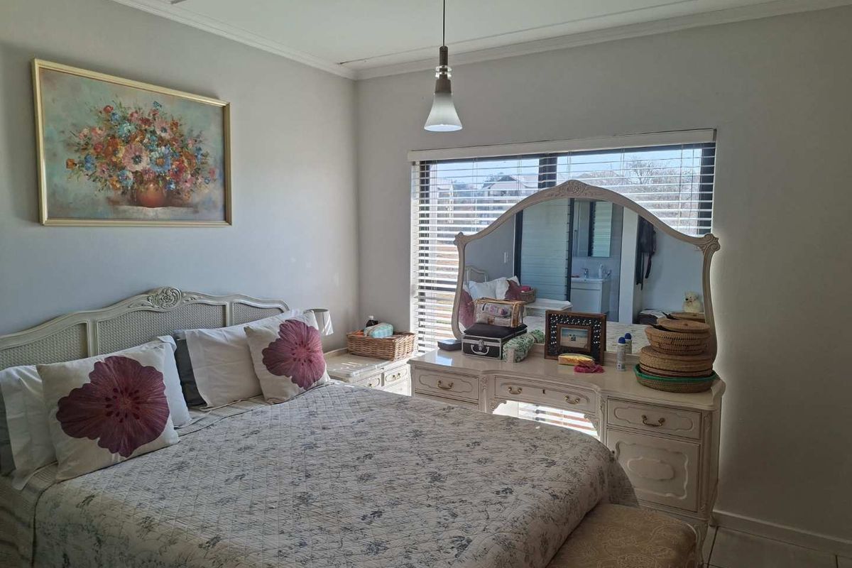 A well-lit bedroom featuring tiled flooring, neutral wall finishes, and large windows fitted with venetian blinds.
