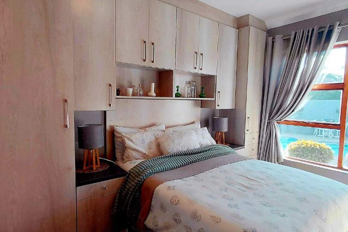 A well-appointed bedroom featuring extensive built-in cabinetry, integrated bedside tables, and a large window providing natural light and a view of the pool area.
