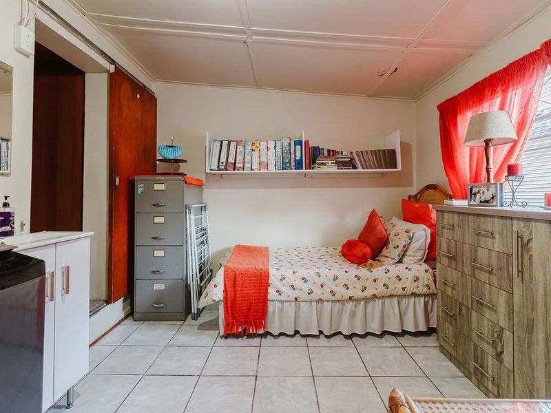 A bedroom featuring tiled flooring, built-in shelving, and a small integrated vanity sink area, requiring cosmetic updates to improve its overall condition.