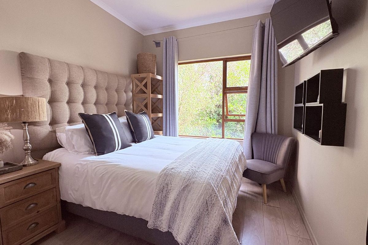 A well-maintained bedroom featuring laminate flooring, neutral wall tones, and a large window providing natural light and garden views.