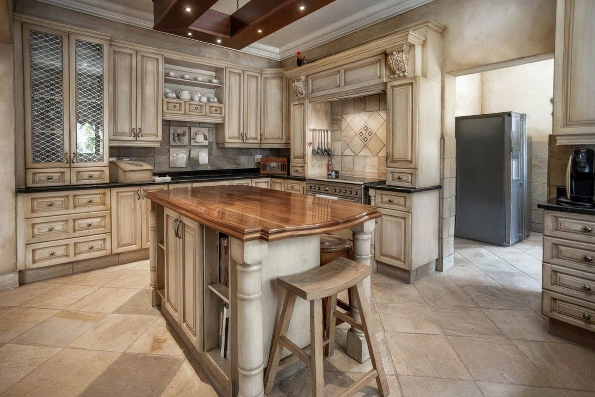 A traditional kitchen featuring custom cabinetry, a central wooden island, stone tile flooring, and a built-in stove with a decorative range hood.