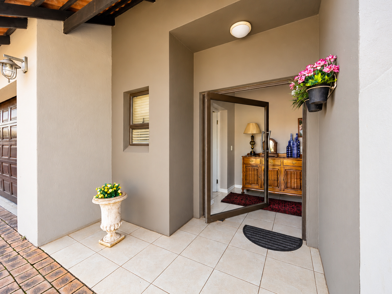 A welcoming front entrance featuring a tiled porch, a modern pivot door, and an integrated garage, providing a clean and well-maintained exterior facade.