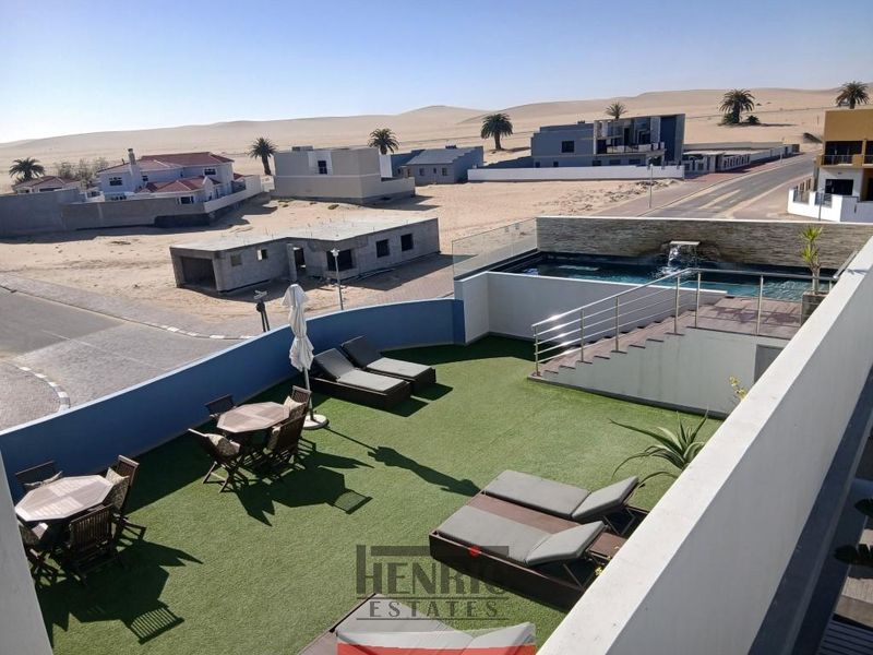 Elevated rooftop terrace featuring a private swimming pool, water feature, glass balustrades, and artificial turf with expansive desert and neighbourhood views.