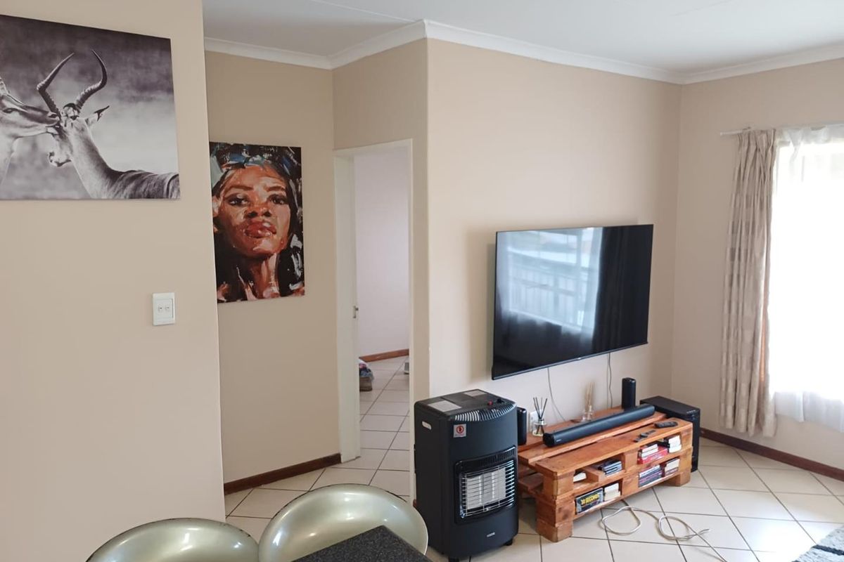 A living room area featuring tiled flooring, neutral wall tones, and a wall-mounted television setup with access to an adjacent hallway.