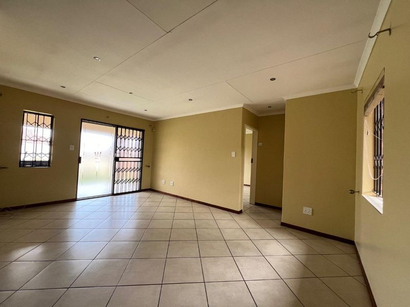 A spacious, empty living area featuring neutral tiled flooring, recessed lighting, and secure access via a sliding glass door with security gate.
