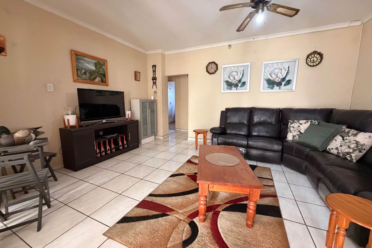 A spacious living room featuring neutral walls, ceramic floor tiles, and a ceiling fan, providing a comfortable and functional living area.