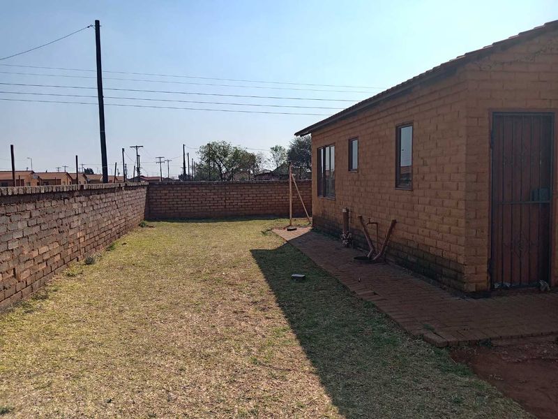 Rear exterior view of the property featuring a brick facade, paved walkway, and a surrounding brick boundary wall with a grassed yard area.