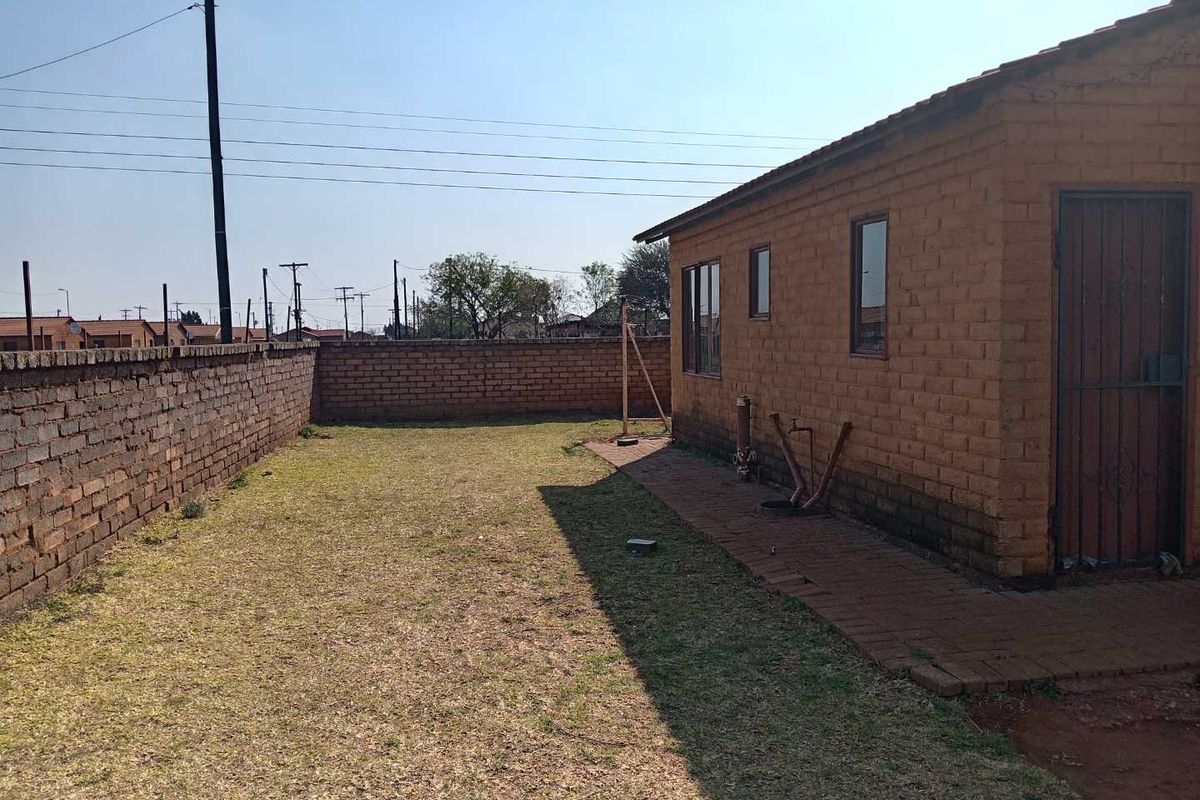 Rear exterior view of the property featuring a brick facade, paved walkway, and a surrounding brick boundary wall with a grassed yard area.