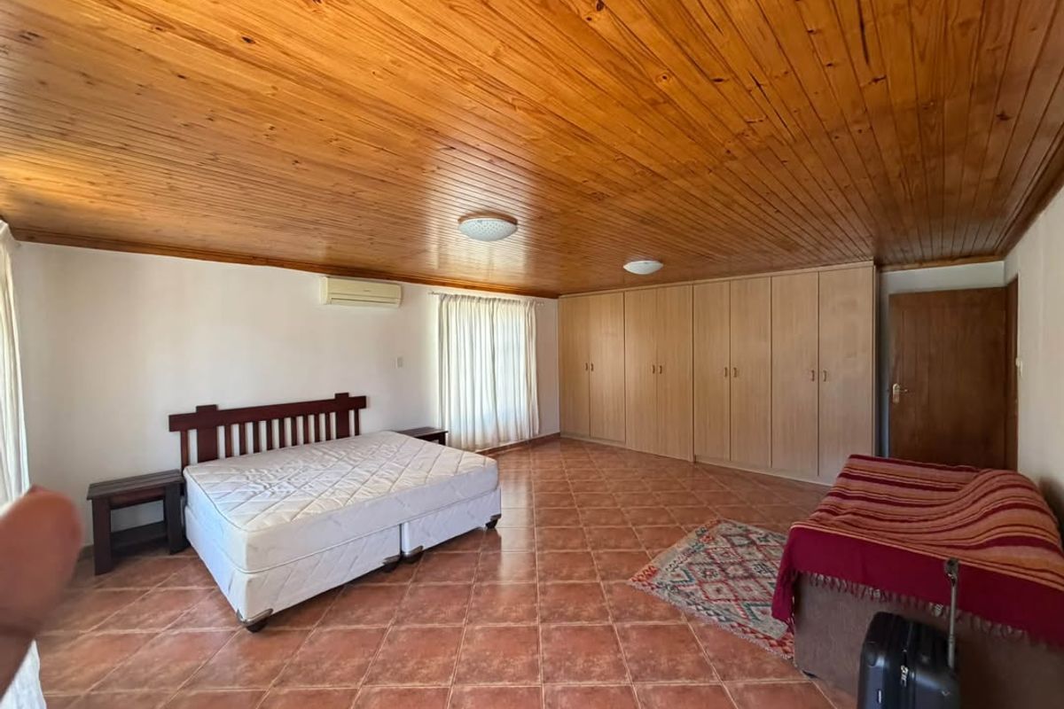 Spacious bedroom featuring a warm timber-clad ceiling, extensive built-in storage cupboards, tiled flooring, and a wall-mounted air conditioning unit.