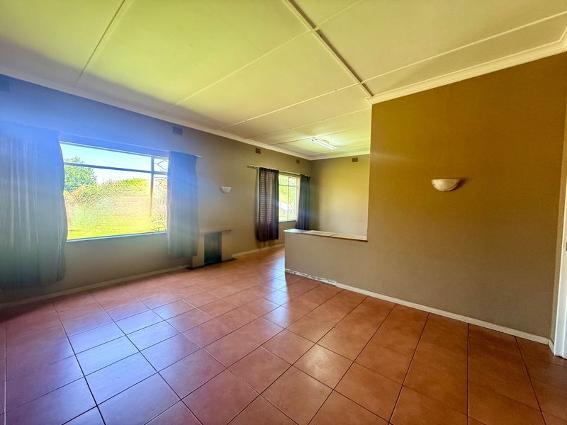 An empty living room featuring tiled flooring, wall sconces, and a partition wall, offering a blank canvas for potential renovation and interior design updates.