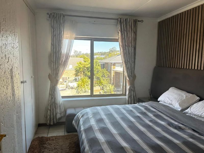 A well-lit bedroom featuring built-in wardrobes, modern slatted wood wall paneling, and tiled flooring with a view of the surrounding neighborhood.