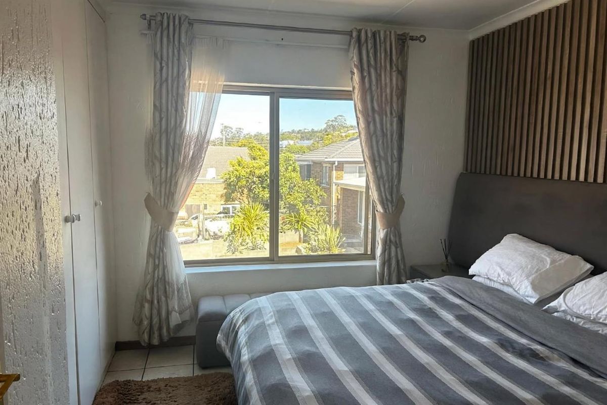 A well-lit bedroom featuring built-in wardrobes, modern slatted wood wall paneling, and tiled flooring with a view of the surrounding neighborhood.