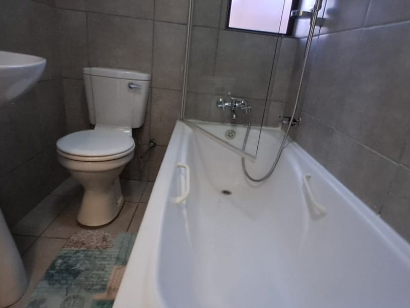 A functional bathroom featuring a pedestal basin, toilet, and a bathtub with a shower mixer, finished with neutral wall and floor tiles.