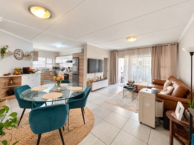An open-plan living, dining, and kitchen area featuring tiled flooring, modern cabinetry, and direct access to an outdoor patio through sliding glass doors.