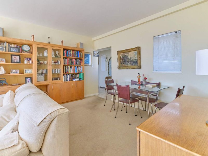 A living and dining area featuring neutral walls, carpeted flooring, and a large built-in wooden shelving unit.