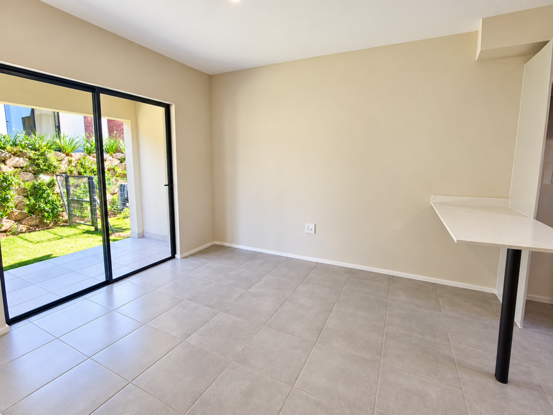 Bright open-plan living area featuring neutral tiled flooring, a modern stone breakfast bar, and large sliding glass doors leading to a private patio.