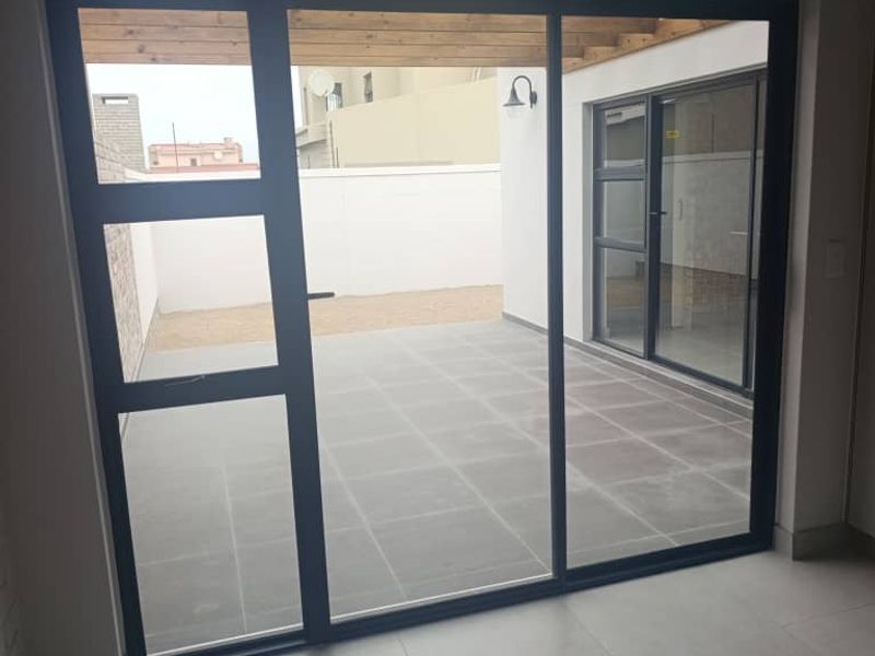 A modern, tiled patio area featuring a timber pergola and large sliding glass doors, providing a seamless transition to the outdoor space.
