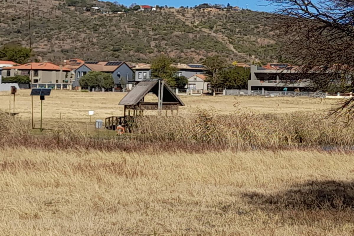 A view of a vacant residential plot featuring a small wooden gazebo, solar panel installation, and surrounding natural vegetation.