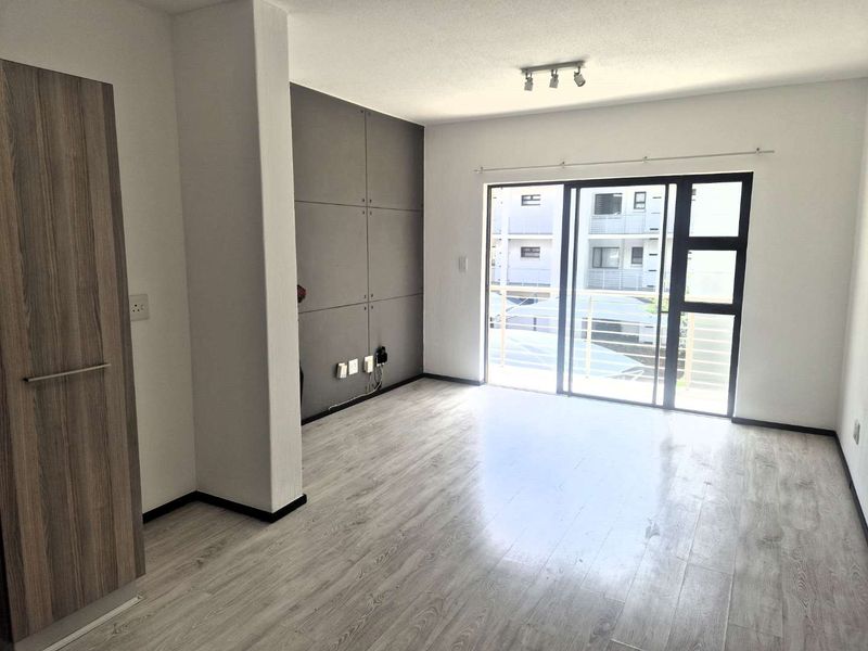 Bright and modern living area featuring light laminate flooring, a feature wall, and large sliding glass doors leading to an outdoor space.