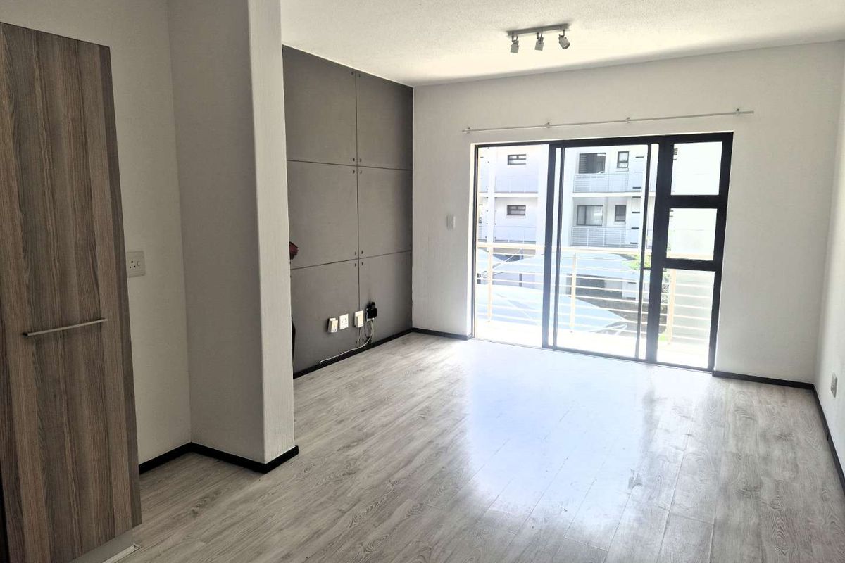 Bright and modern living area featuring light laminate flooring, a feature wall, and large sliding glass doors leading to an outdoor space.