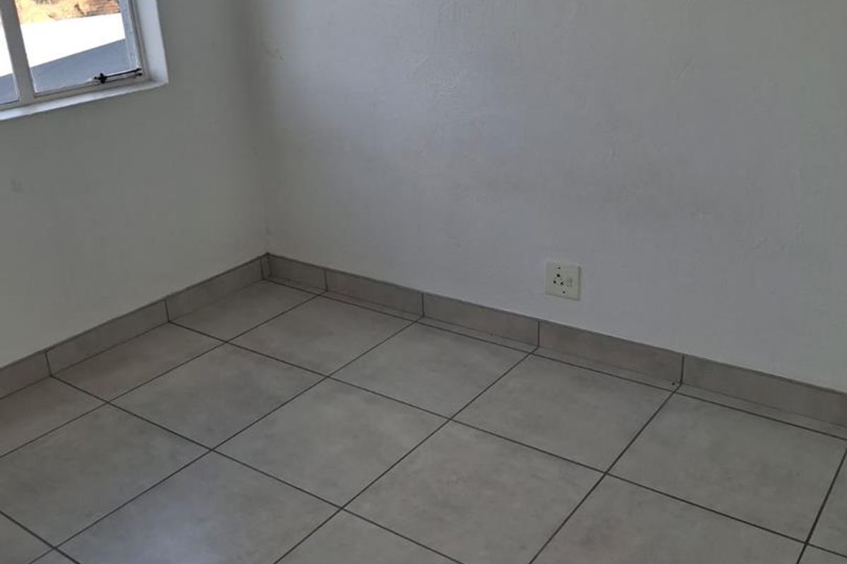 A vacant bedroom featuring neutral ceramic floor tiles, white walls, and a window providing natural light.