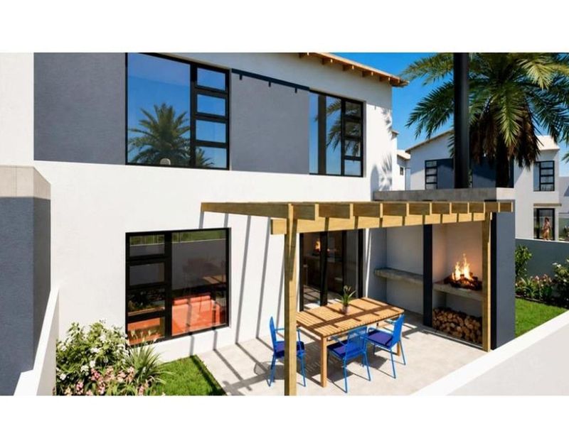 Rear exterior view of a modern townhouse featuring a paved patio, timber pergola, and a built-in outdoor braai area.