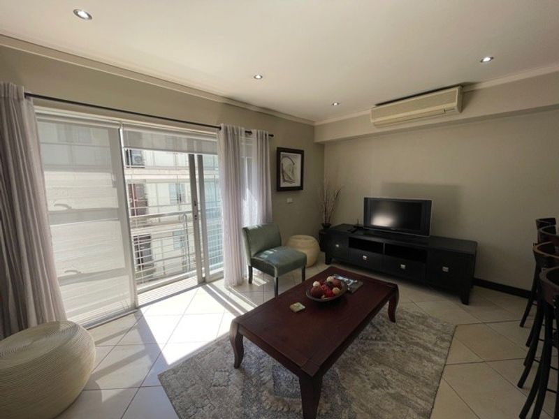 A well-lit living room featuring tiled flooring, recessed downlighting, a wall-mounted air conditioning unit, and large sliding glass doors leading to a balcony.