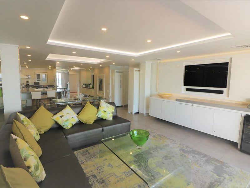 Spacious open-plan living area featuring modern recessed and cove lighting, sleek built-in media cabinetry, and a seamless transition to the contemporary kitchen.