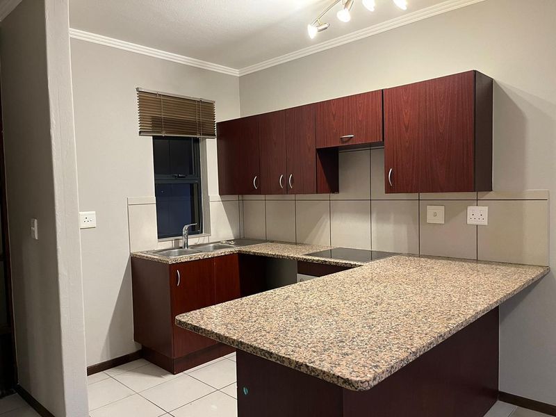 A functional kitchen featuring dark wood-look cabinetry, granite countertops, a built-in electric hob, and neutral tiled flooring and backsplash.
