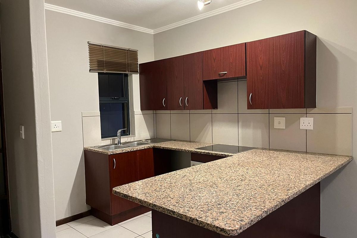 A functional kitchen featuring dark wood-look cabinetry, granite countertops, a built-in electric hob, and neutral tiled flooring and backsplash.