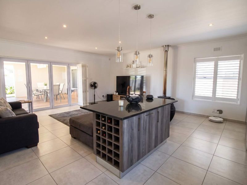 Spacious open-plan living area featuring a modern kitchen island with built-in wine storage, a sleek fireplace, and large sliding doors leading to the patio.