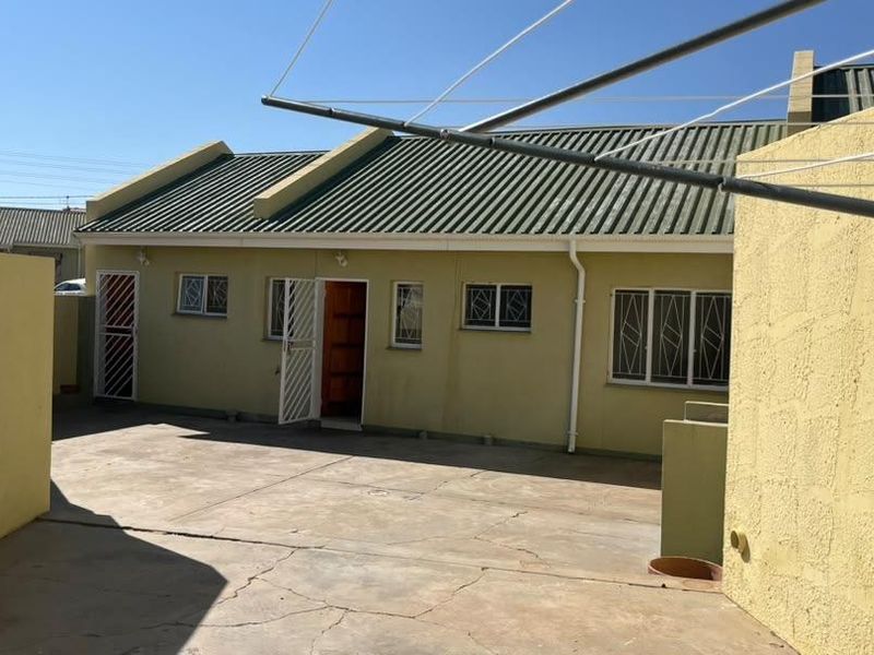 Rear exterior view of the townhouse featuring a paved courtyard, security gates, and security bars on the windows.